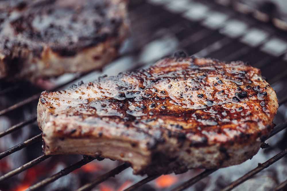 selective focus of juicy spicy steak grilling on barbecue grid with smoke